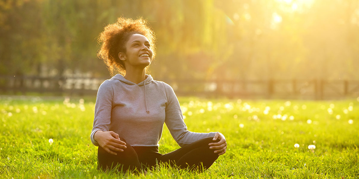Happy young woman sitting outdoors in yoga position.